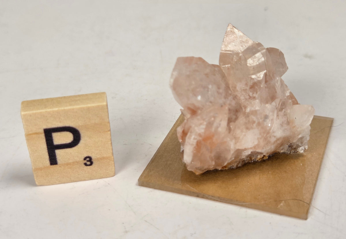 pink colored calcite specimen with a scrabble tile against a marbled background