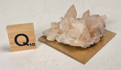 pink colored calcite specimen with a scrabble tile against a marbled background