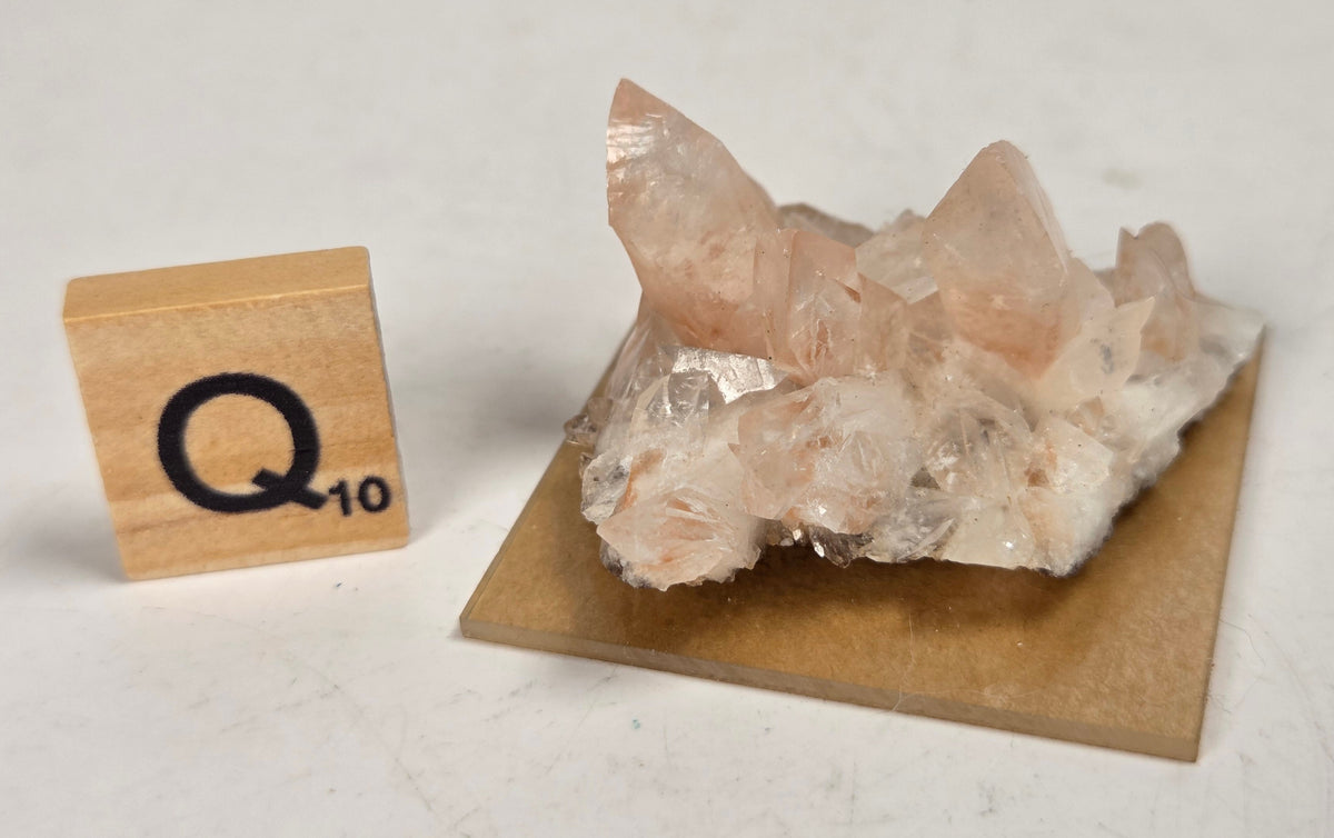 pink colored calcite specimen with a scrabble tile against a marbled background