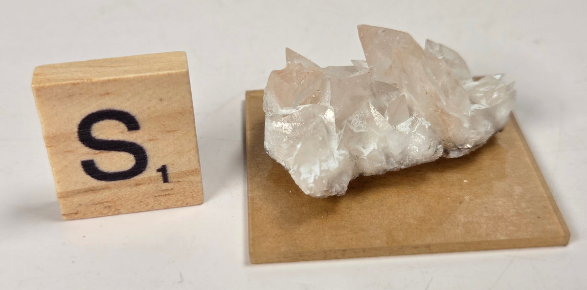 pink colored calcite specimen with a scrabble tile against a marbled background