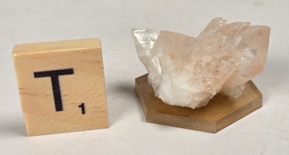 pink colored calcite specimen with a scrabble tile against a marbled background
