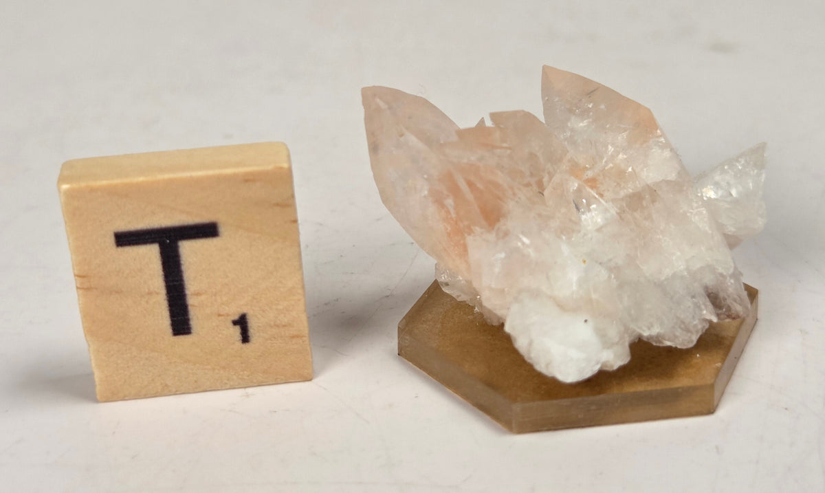 pink colored calcite specimen with a scrabble tile against a marbled background