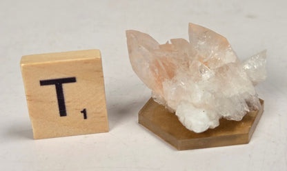 pink colored calcite specimen with a scrabble tile against a marbled background