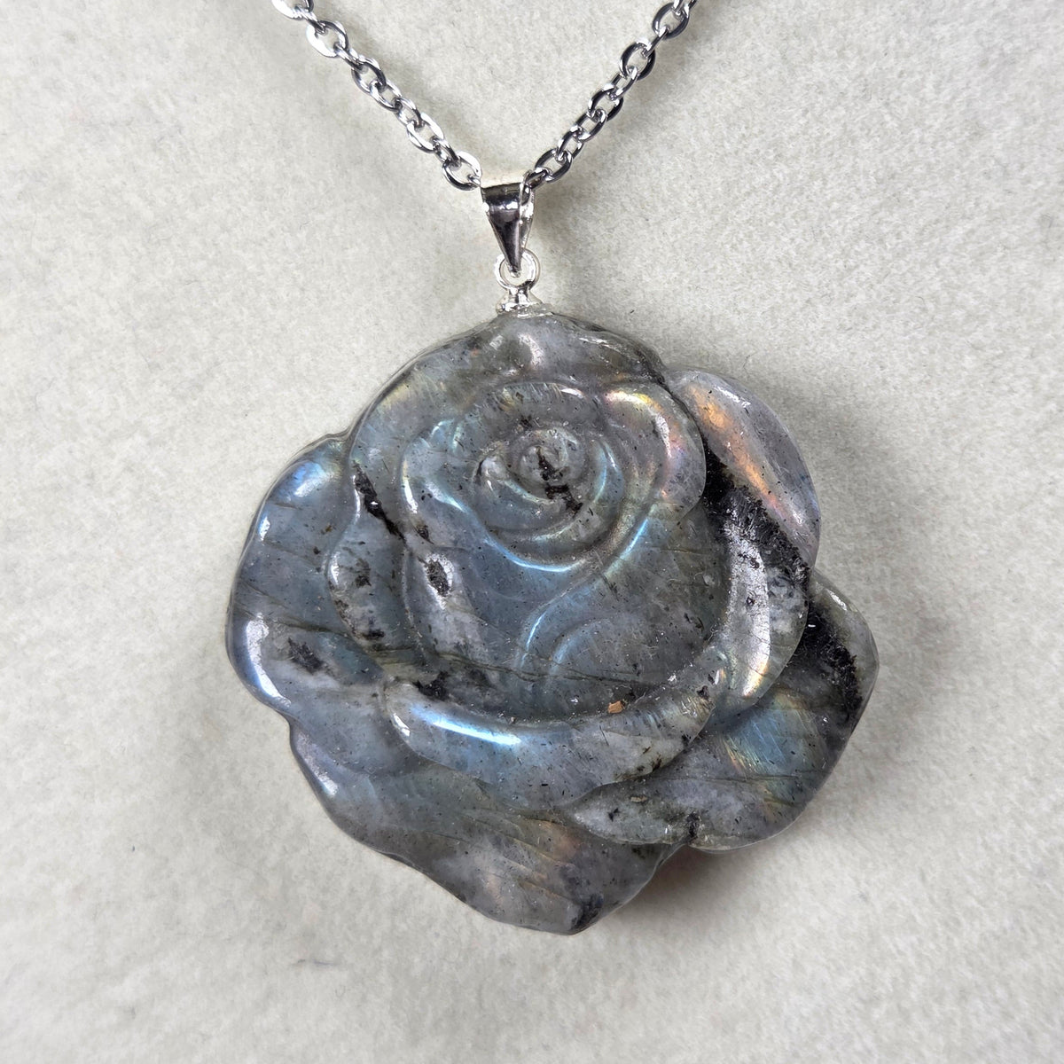 Grey crystal rose shaped pendant with rainbow flash on a silver chain against a tan background