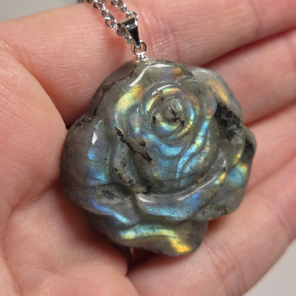 Hand holding a grey crystal rose shaped pendant with rainbow flash on a silver chain against a white background