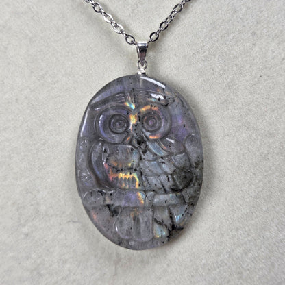 Grey crystal owl shaped pendant with rainbow flash on a silver chain against a tan background