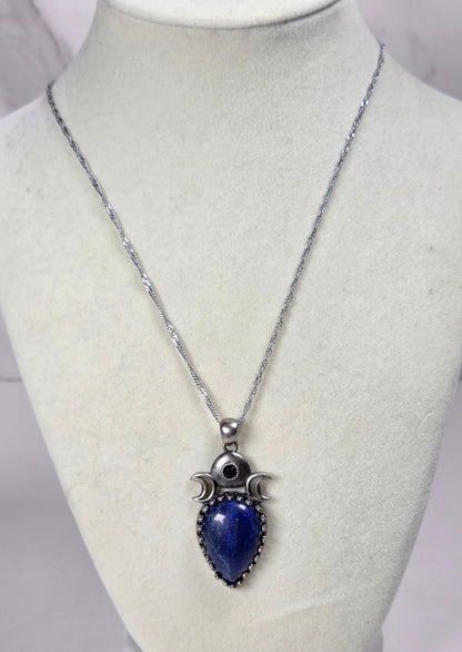 Silver pendant withe a blue crystal cabachon with silver moon accents, on a silver chain against a tan background