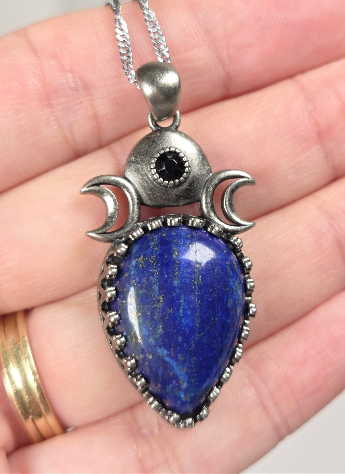 Hand holding a silver pendant withe a blue crystal cabachon with silver moon accents, on a silver chain against a white background