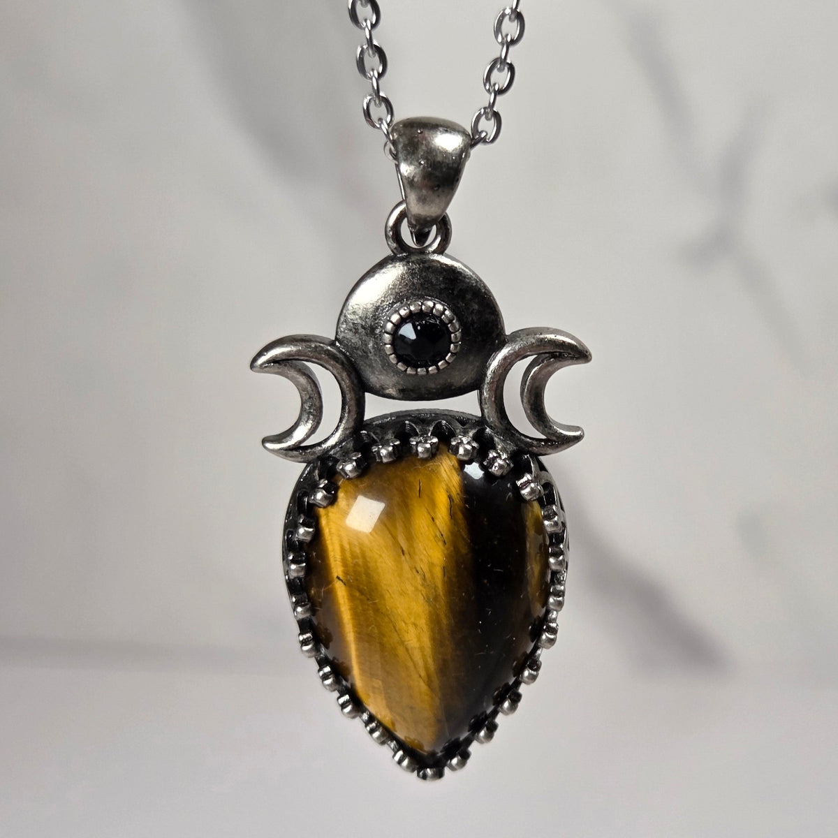 A silver pendant withe a striped brown  crystal cabachon with silver moon accents, on a silver chain against a white background