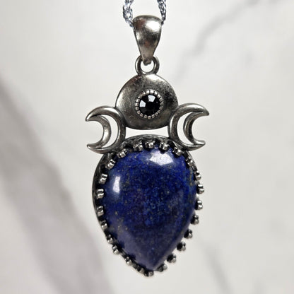A silver pendant withe a blue crystal cabachon with silver moon accents, on a silver chain against a white background