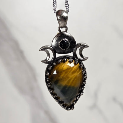 A silver pendant withe a brown and blue  crystal cabachon with silver moon accents, on a silver chain against a white background