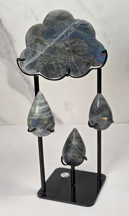 Grey crystal carving of a cloud and rain drops, with various color flashes, on a black stand against a white background
