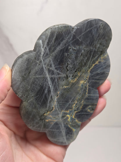Hand holding a grey labradorite carved cloud with yellow coloring against a white background