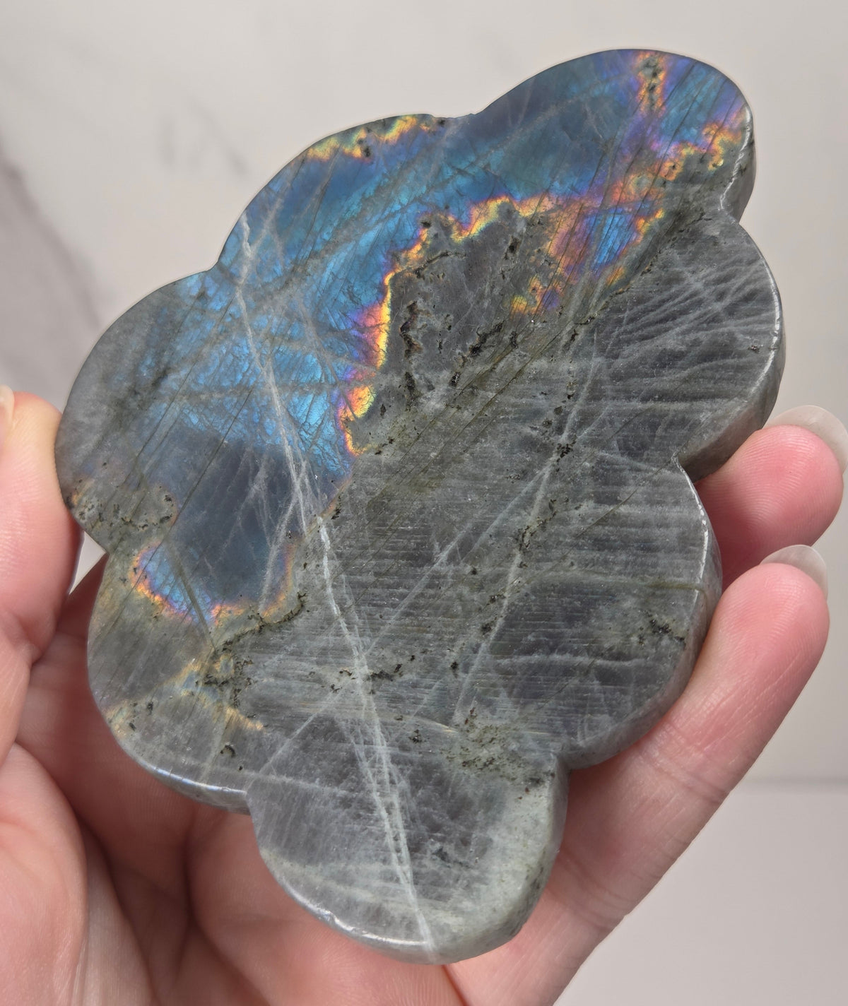 Hand holding a grey labradorite carved cloud with blue coloring against a white background
