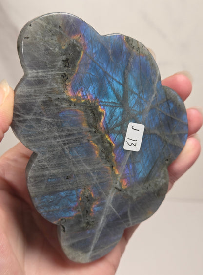 Hand holding a grey labradorite carved cloud with blue and pink coloring against a white background