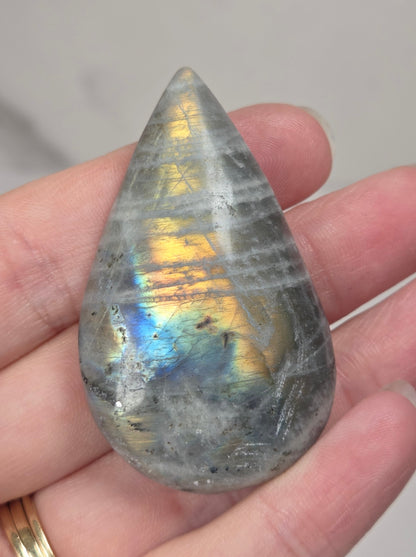 Hand holding a grey labradorite carved raindrop shaped carving with rainbow coloring against a white background