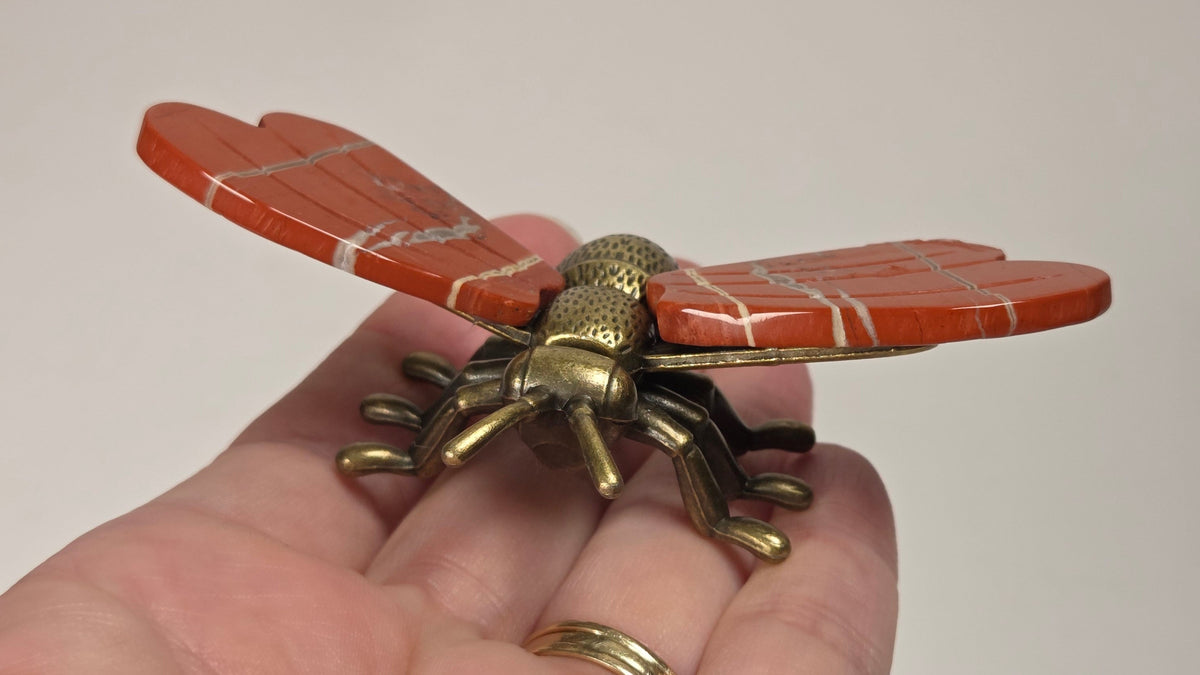 A close-up of a hand holding a vintage-style brass bumblebee brooch. The brooch features detailed wing and body textures with a warm gold and bronze metallic finish.