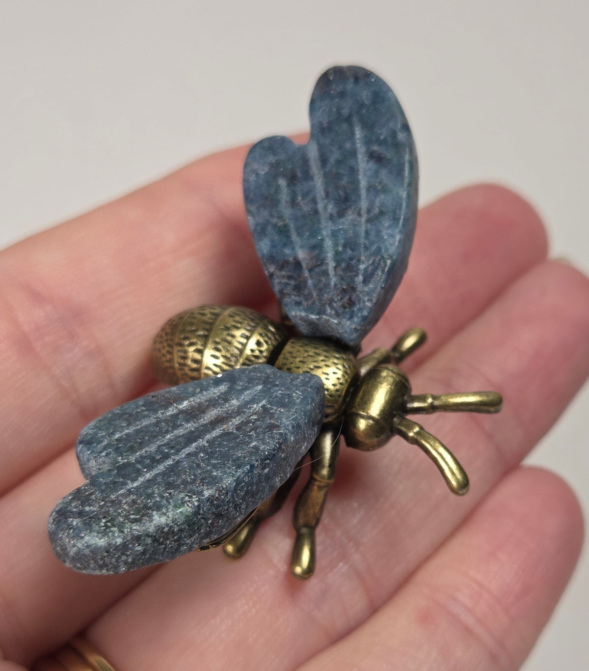A close-up of a hand holding a vintage-style brass bumblebee brooch. The brooch features detailed wing and body textures with a warm gold and bronze metallic finish.