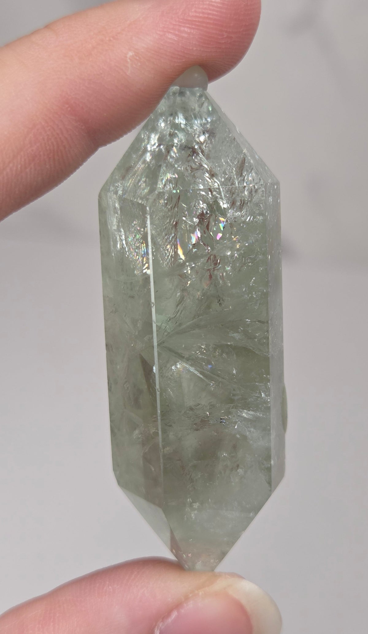 green quartz carved point being held in a hand against a white background