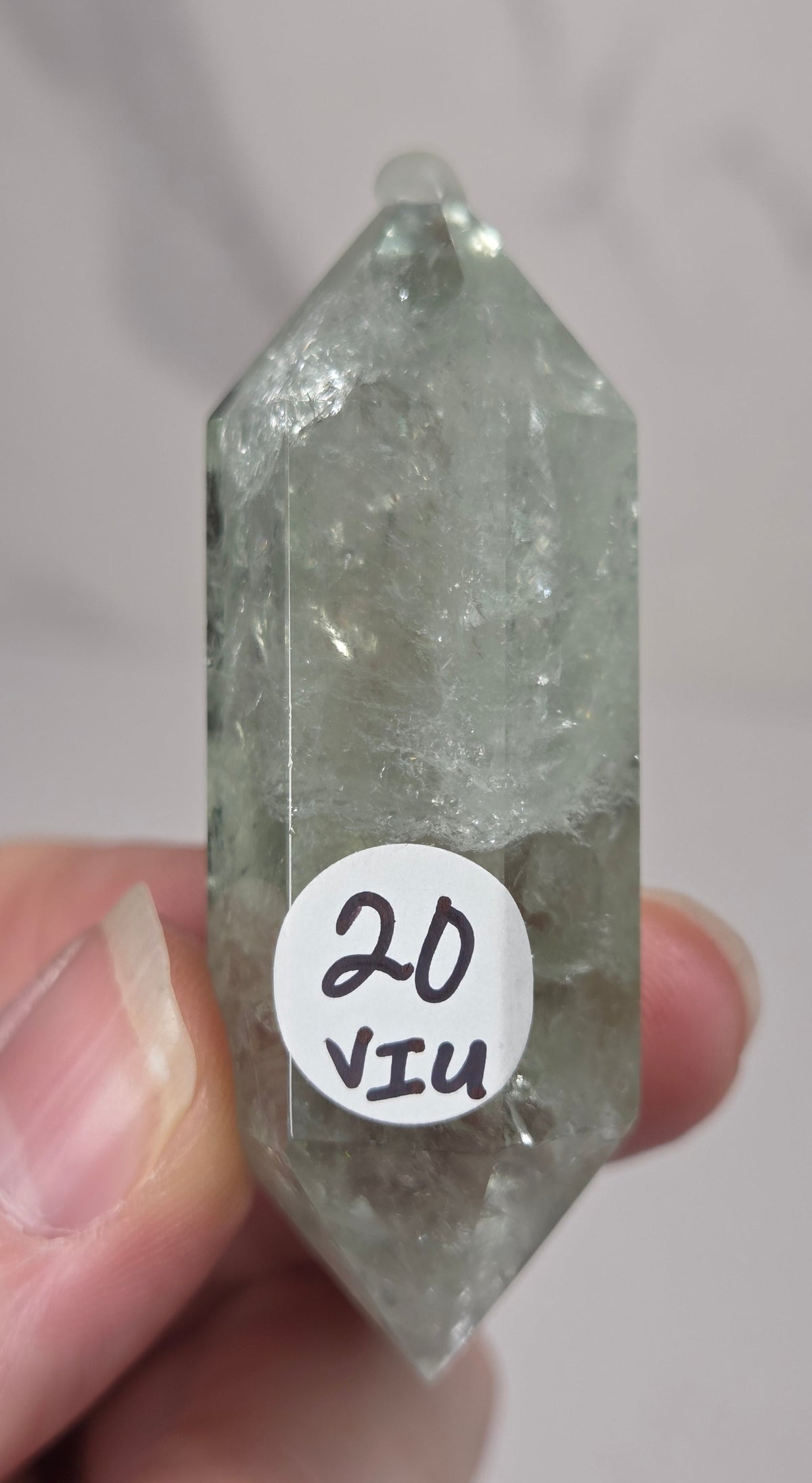 green quartz carved point being held in a hand against a white background