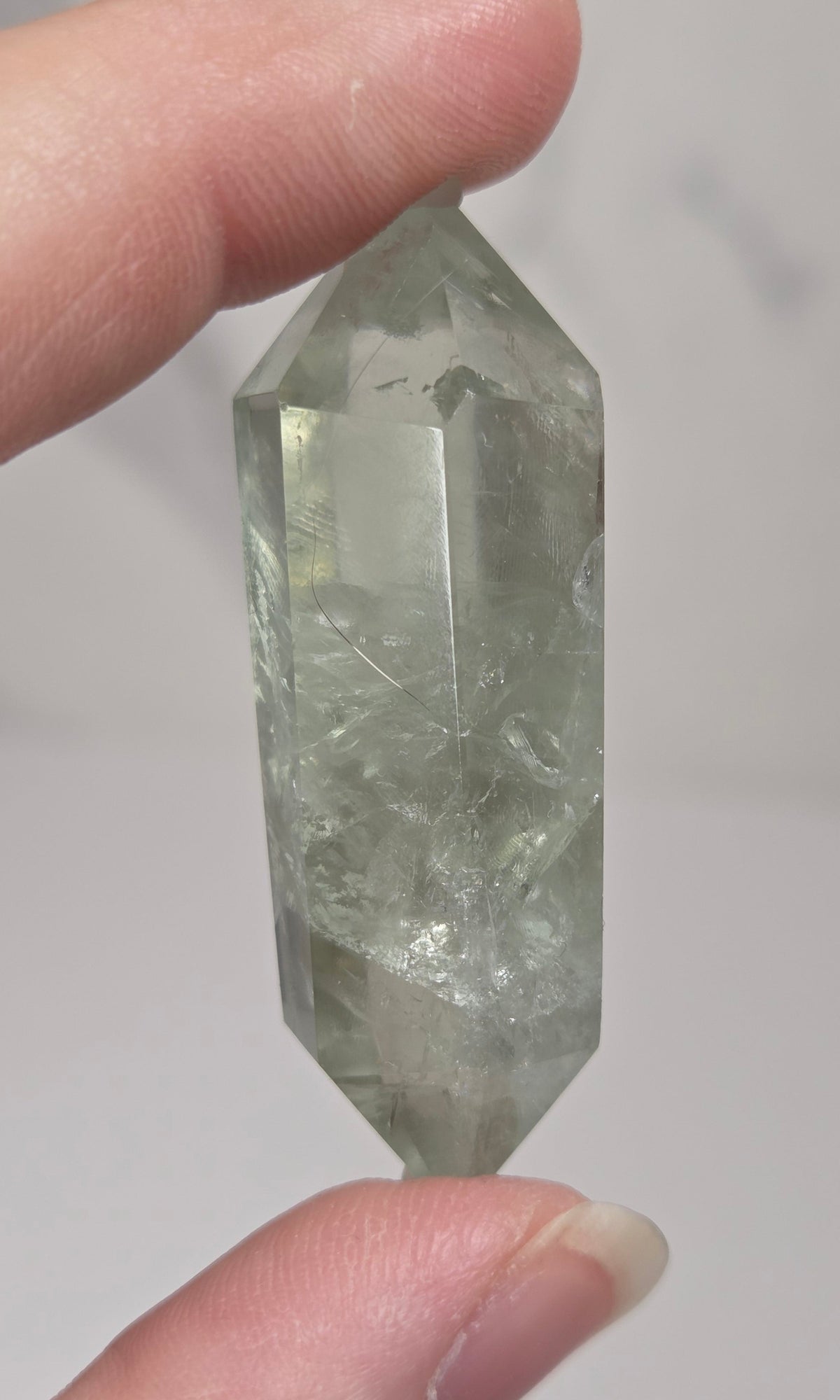 green quartz carved point being held in a hand against a white background