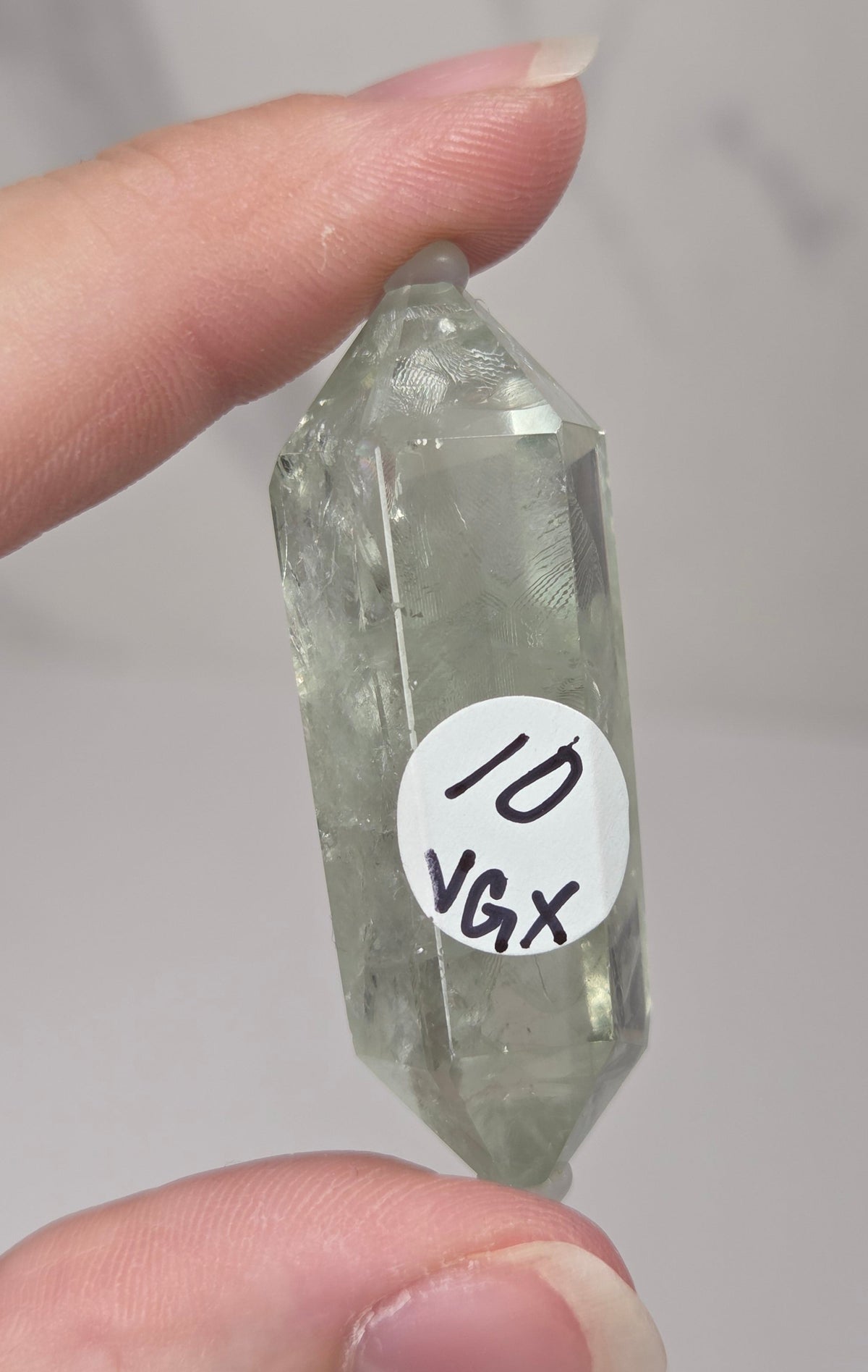 green quartz carved point being held in a hand against a white background