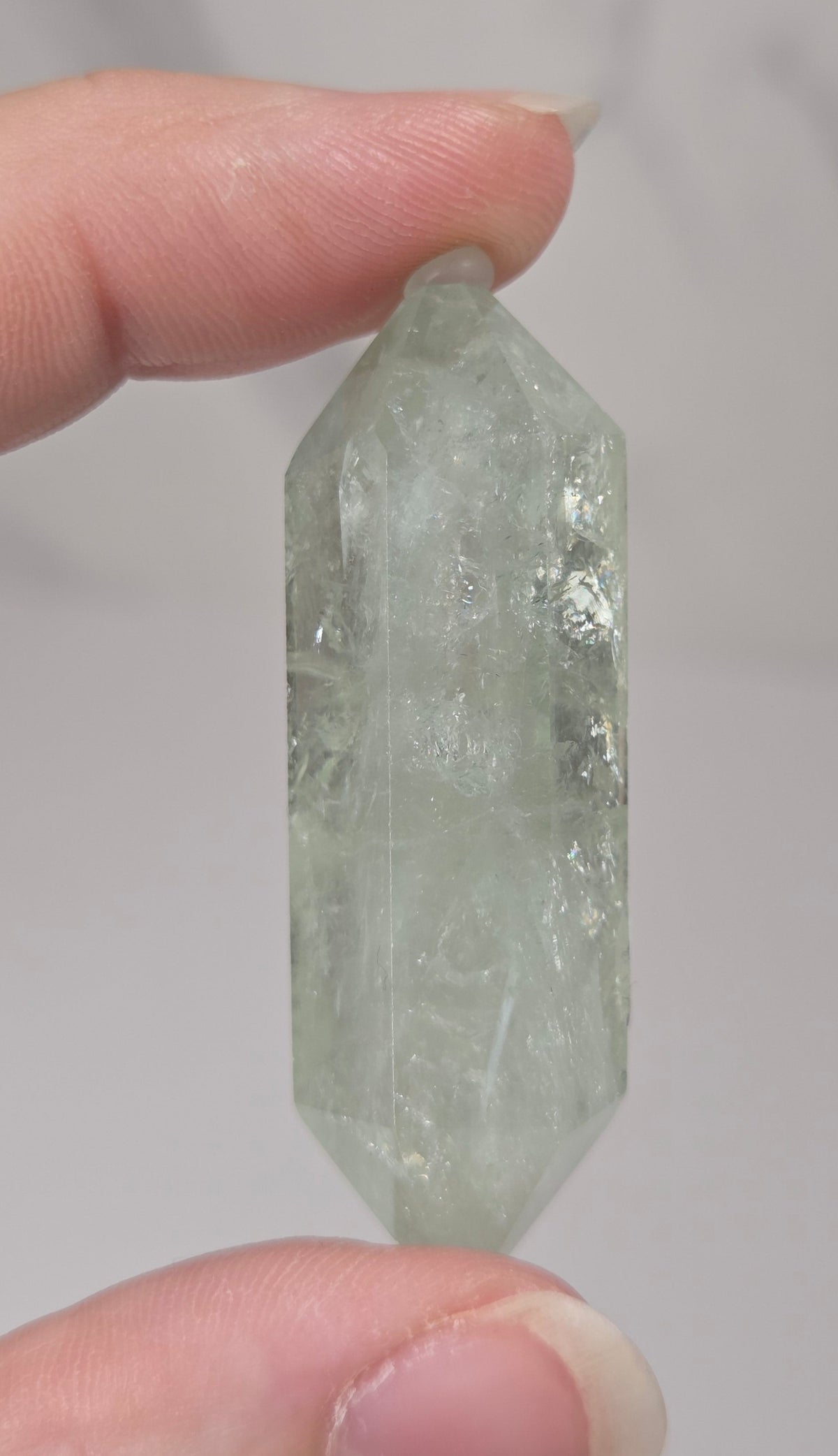 green quartz carved point being held in a hand against a white background