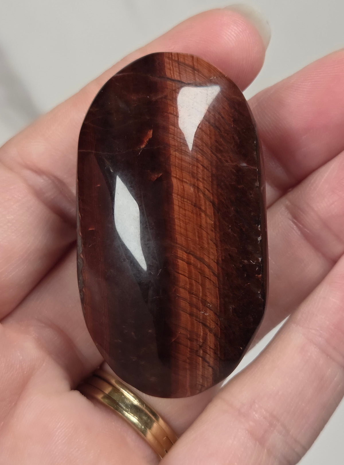 Hand holding a red tigers eye crystal carving with bands against a white background