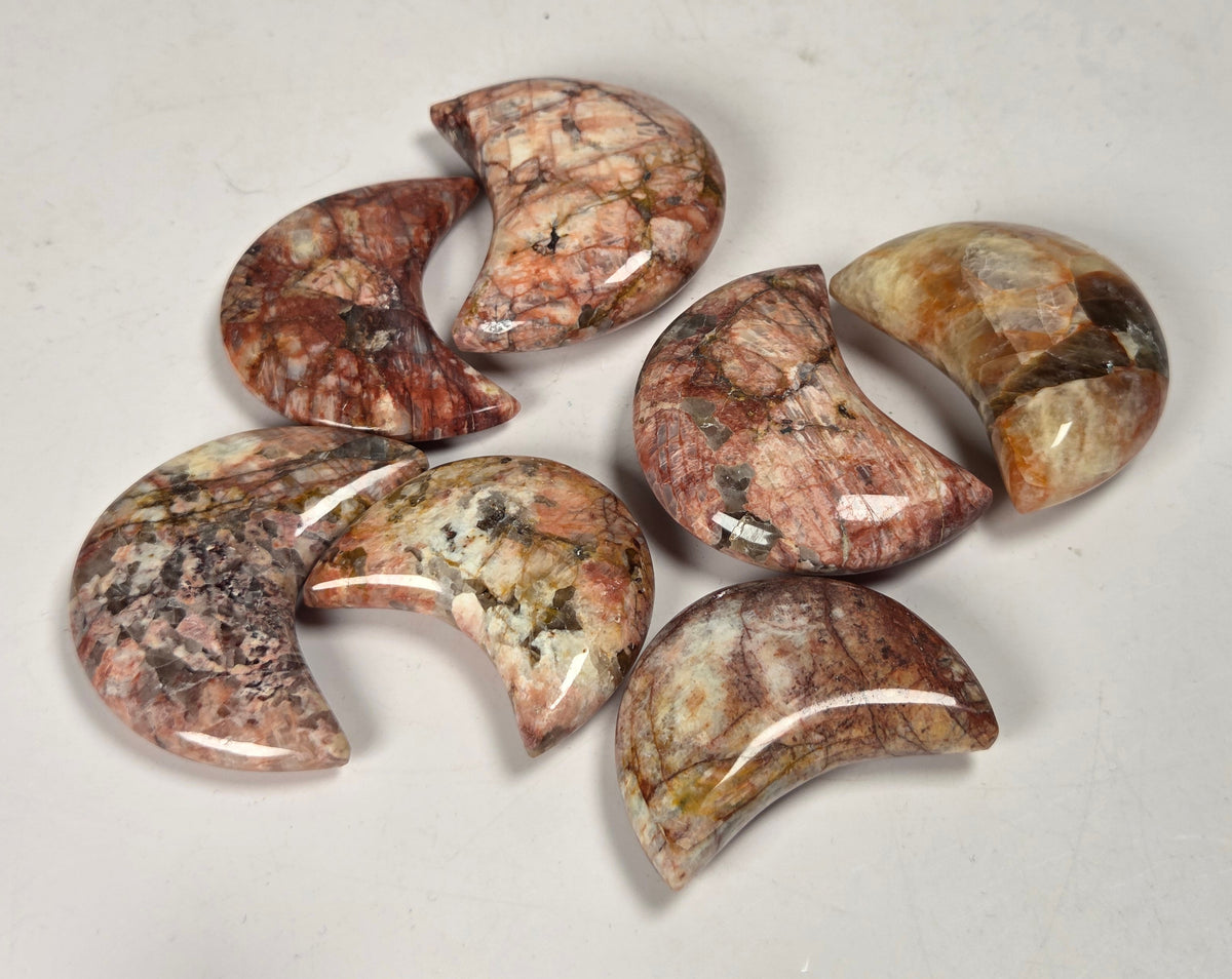 Collection of polished crystal moon carvings with tan, yellow and red coloring against a white background
