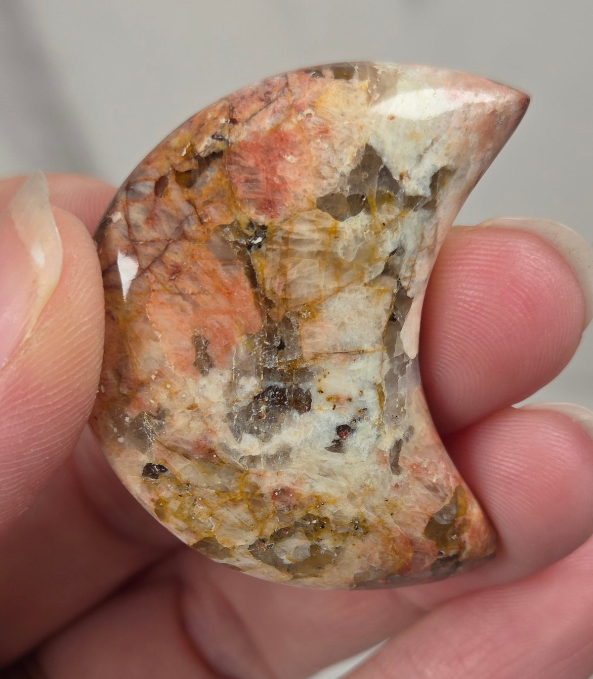 Hand holding a polished crystal moon carving with tan, yellow and red coloring against a white background