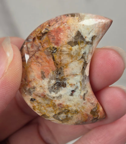 Hand holding a polished crystal moon carving with tan, yellow and red coloring against a white background