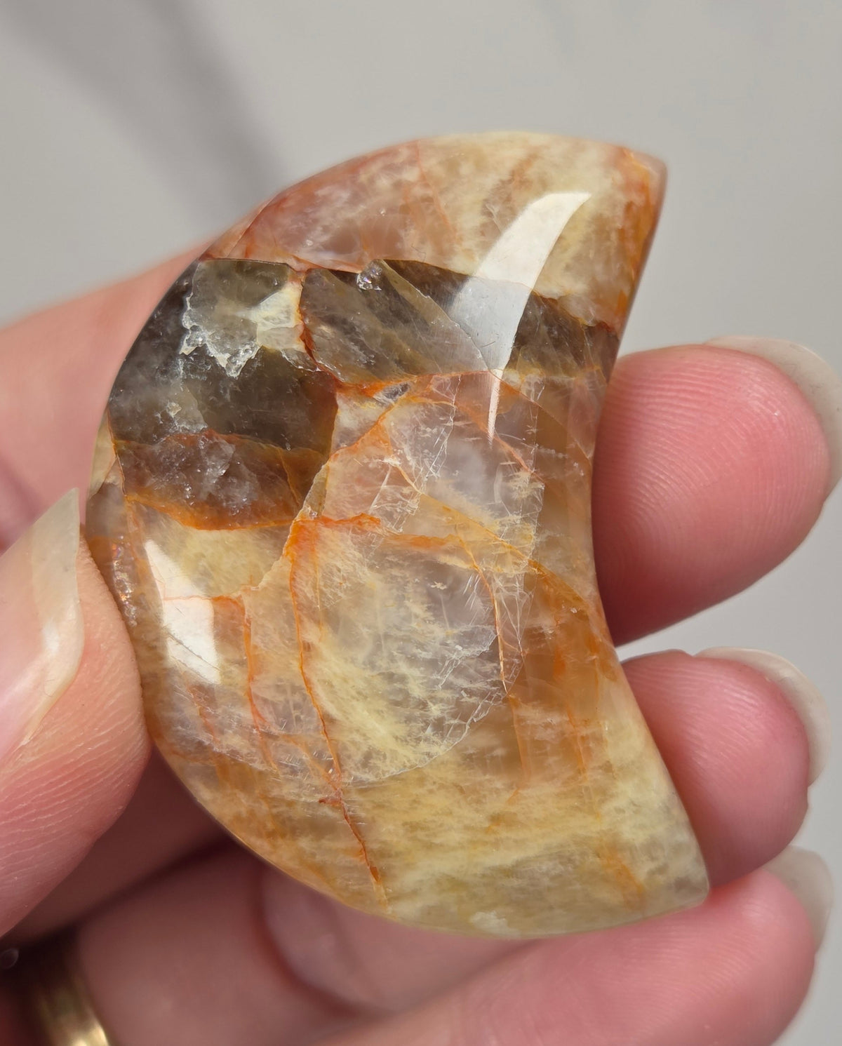 Hand holding a polished crystal moon carving with tan, yellow and red coloring against a white background