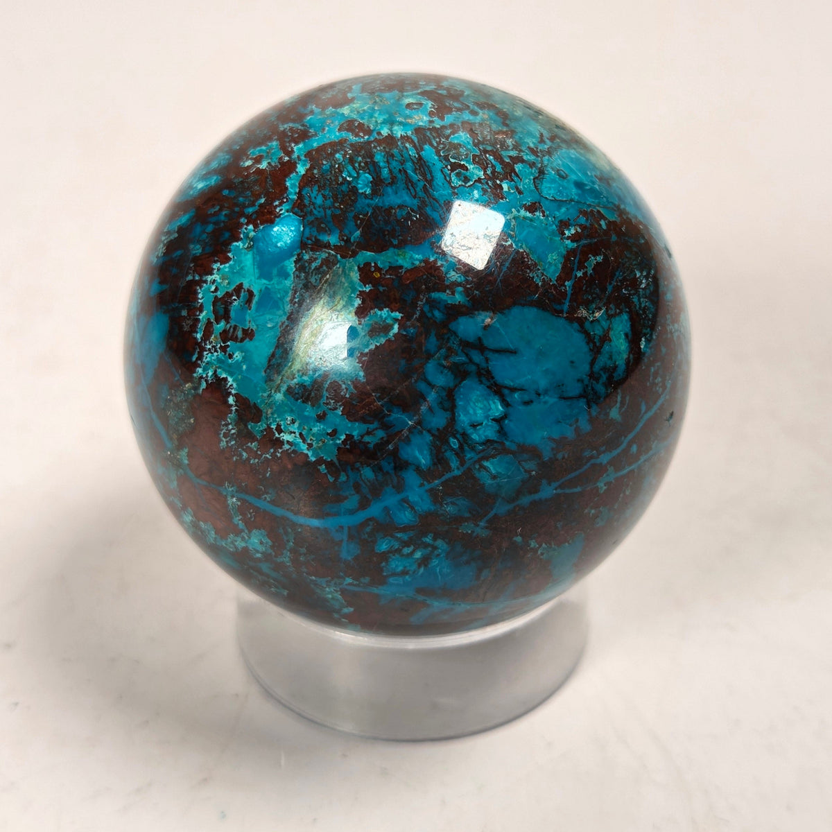 Blue and brown crystal polished sphere carving on an acrylic stand against a white background