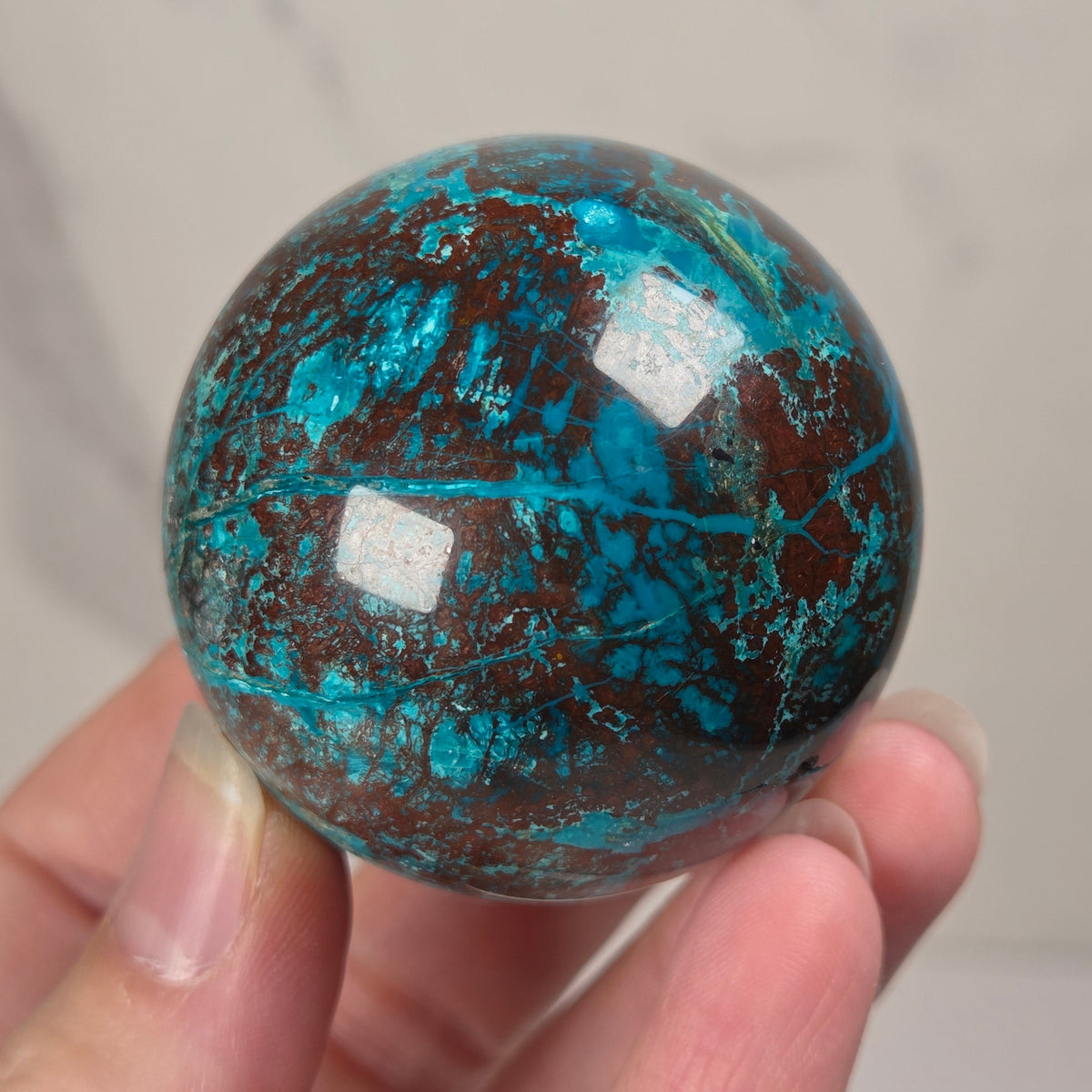 Hand holding a blue and brown crystal polished sphere carving against a white background