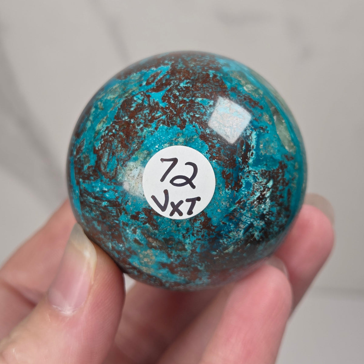 Hand holding a blue and brown crystal polished sphere carving against a white background