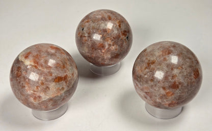 Orange colored crystal sphere carvings on acrylic stands against a white background