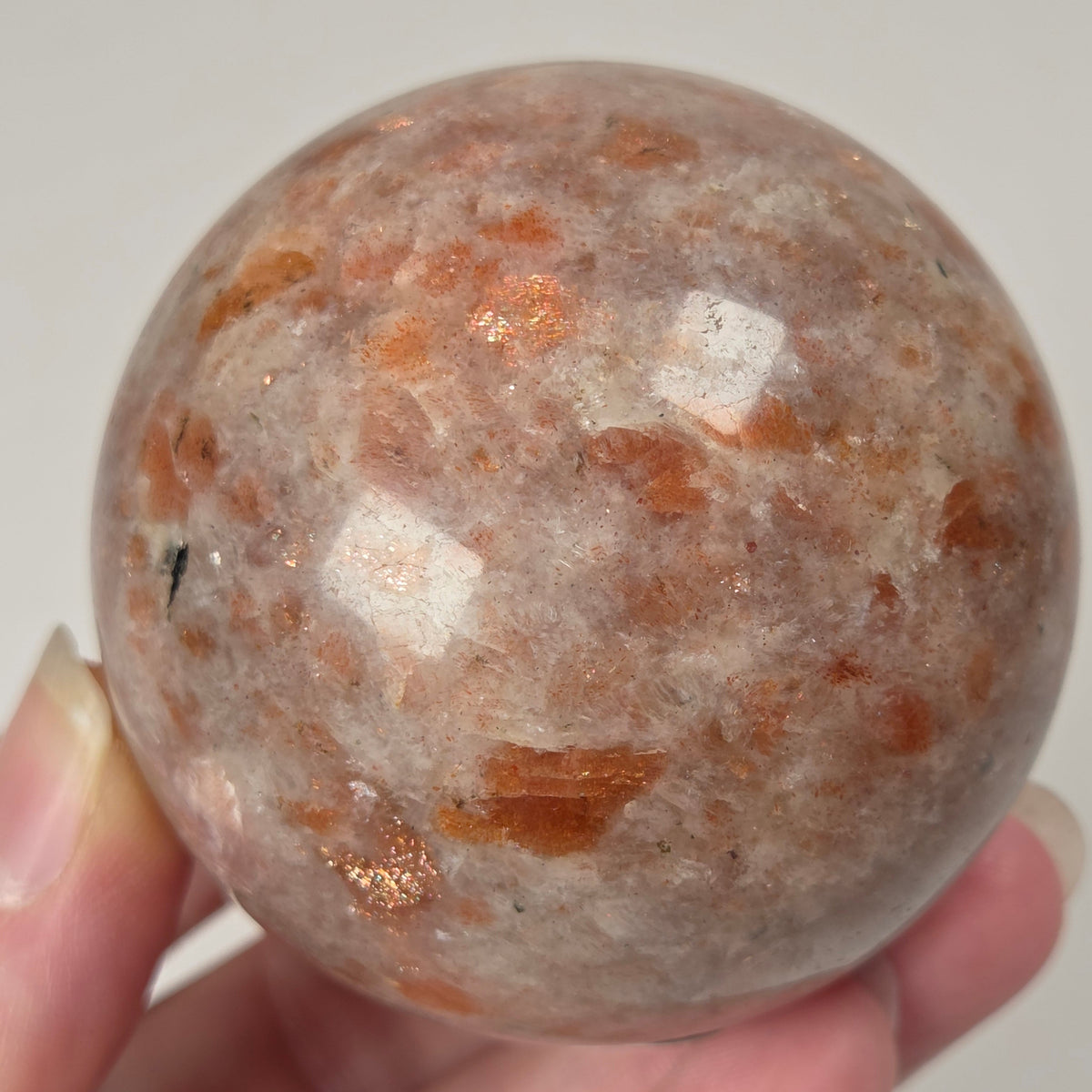 Hand holding an orange colored crystal sphere carving against a white background