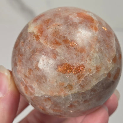 Hand holding an orange colored crystal sphere carving against a white background
