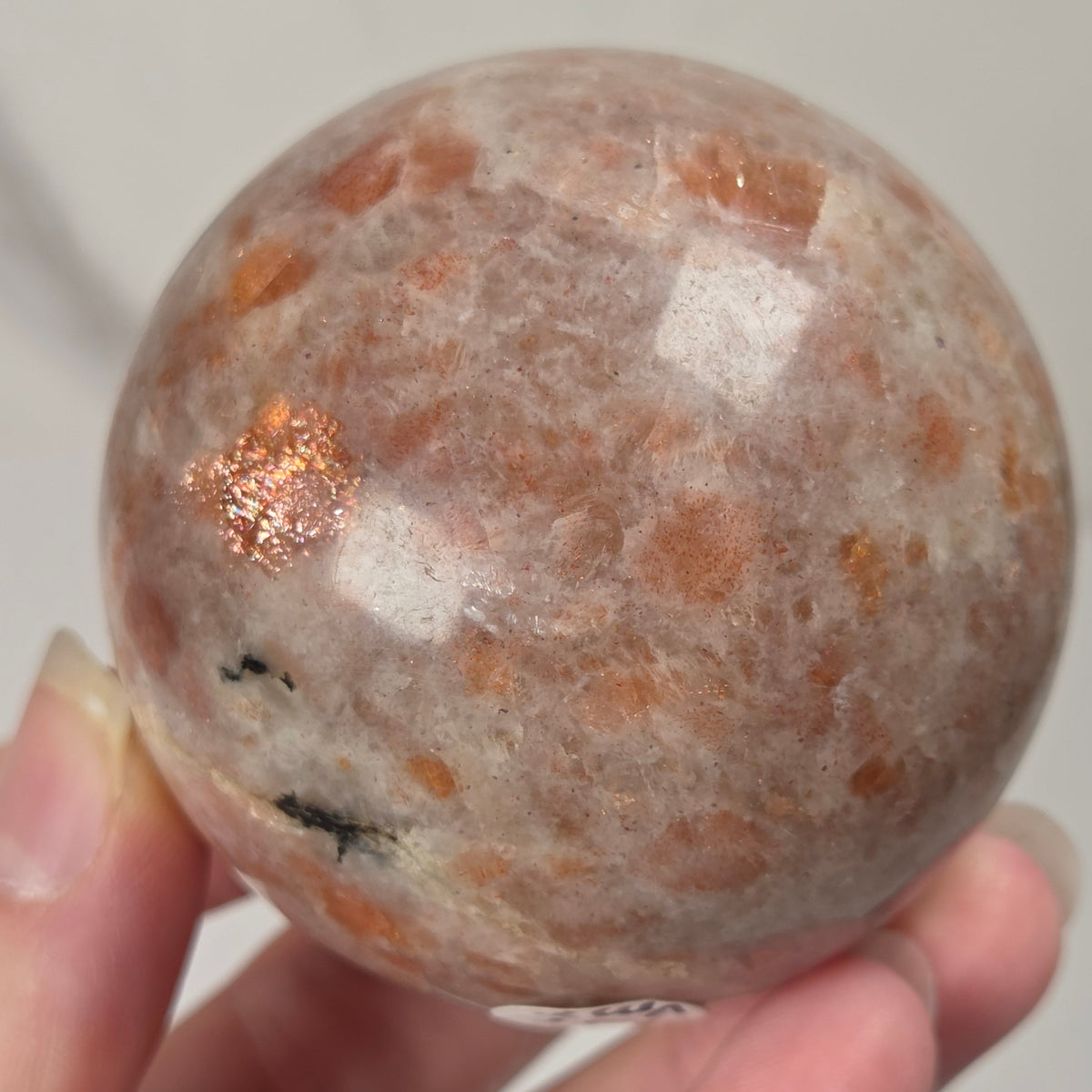 Hand holding an orange colored crystal sphere carving against a white background