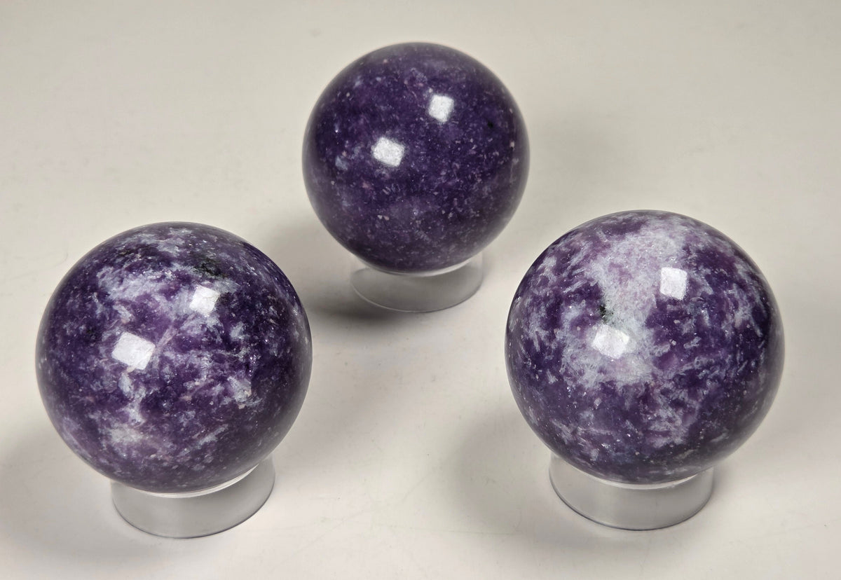 Collection of purple crystal sphere carvings on acrylic stands against a white background