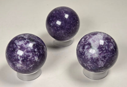 Collection of purple crystal sphere carvings on acrylic stands against a white background