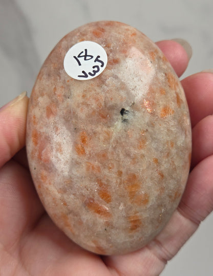 Polished orange sunstone free form carving being held in a hand against a marbled background