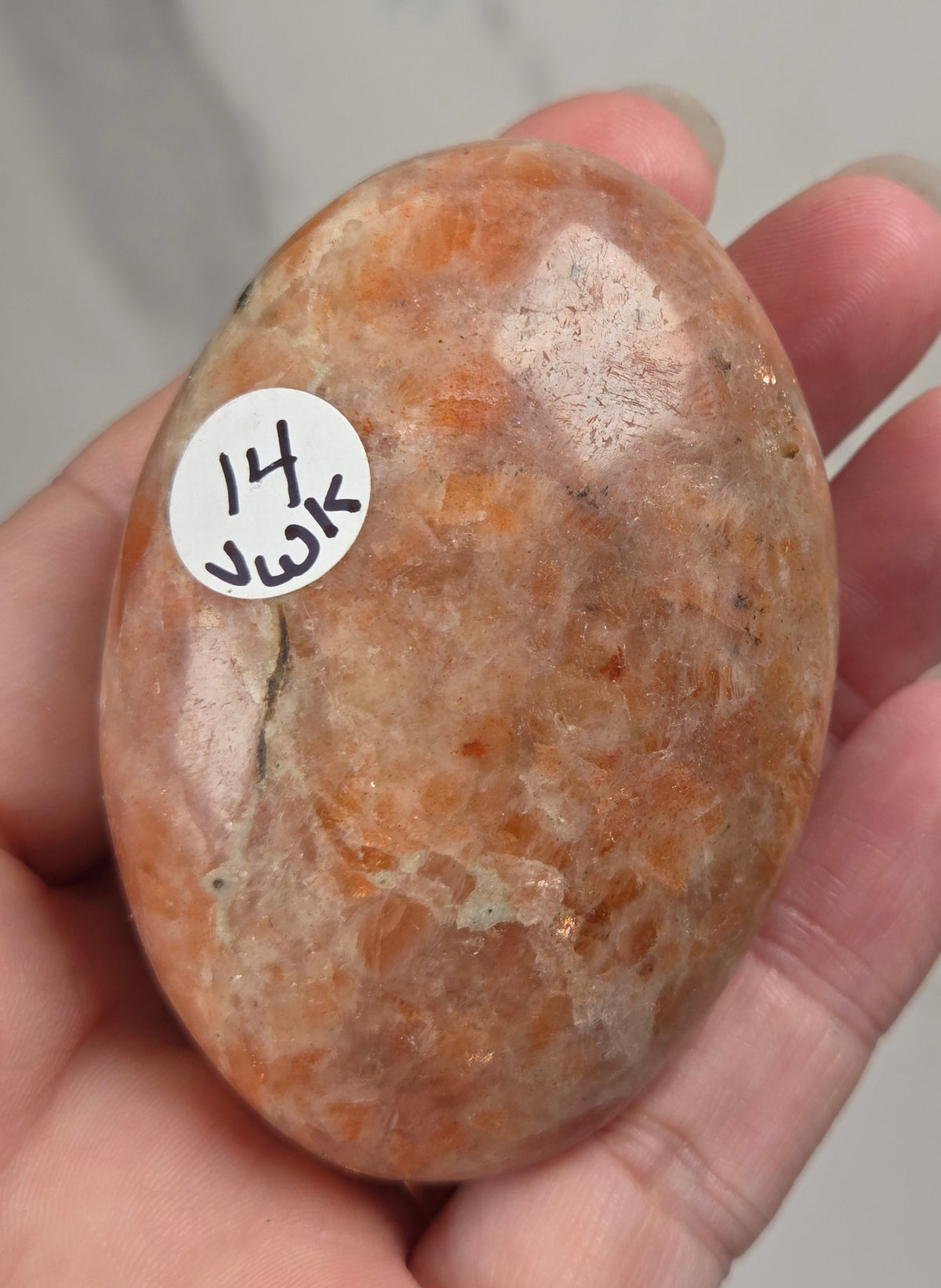 Polished orange sunstone free form carving being held in a hand against a marbled background