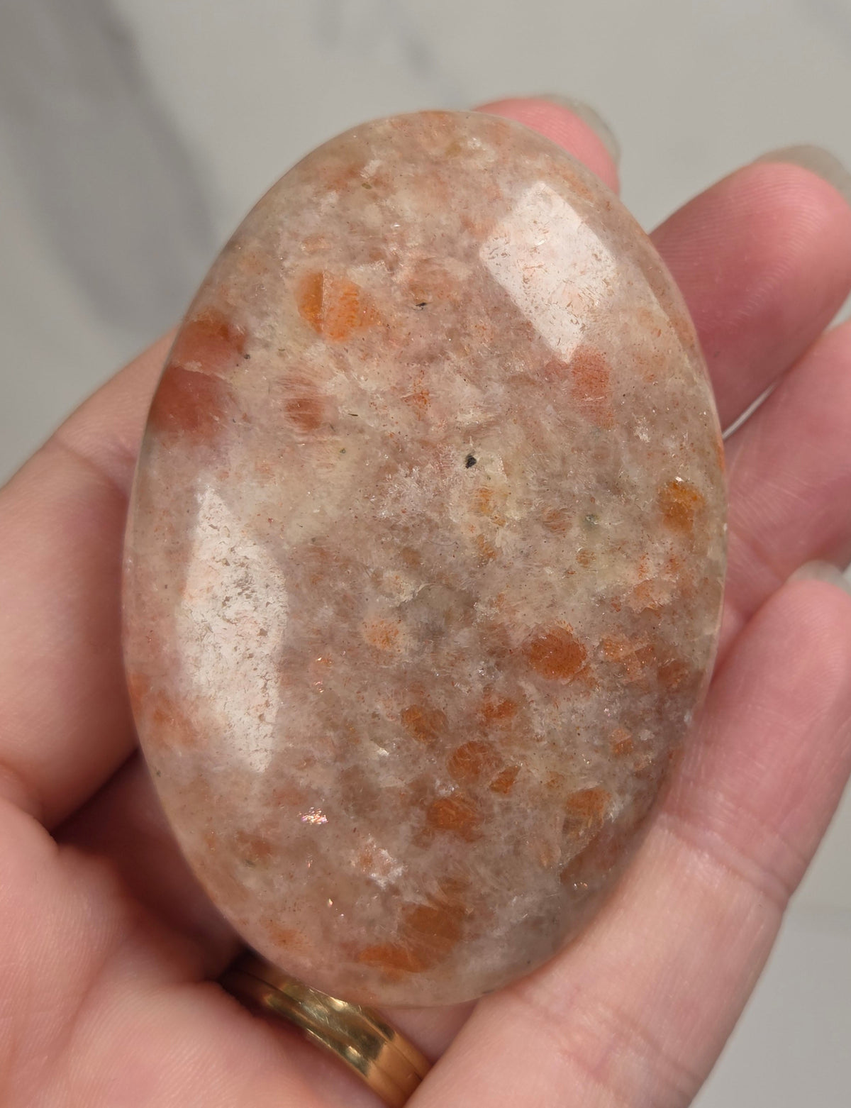 Polished orange sunstone free form carving being held in a hand against a marbled background
