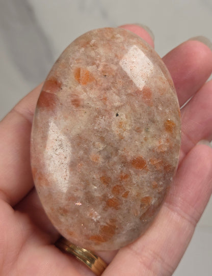 Polished orange sunstone free form carving being held in a hand against a marbled background