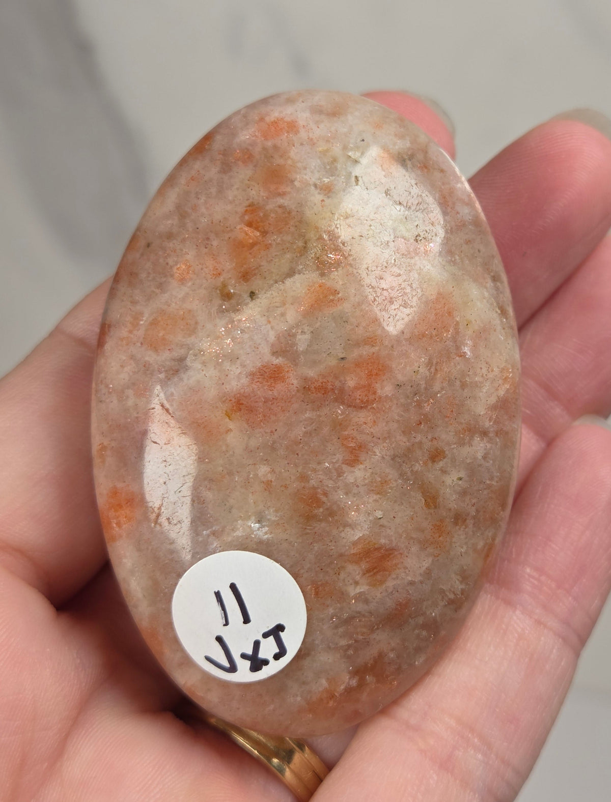 Polished orange sunstone free form carving being held in a hand against a marbled background