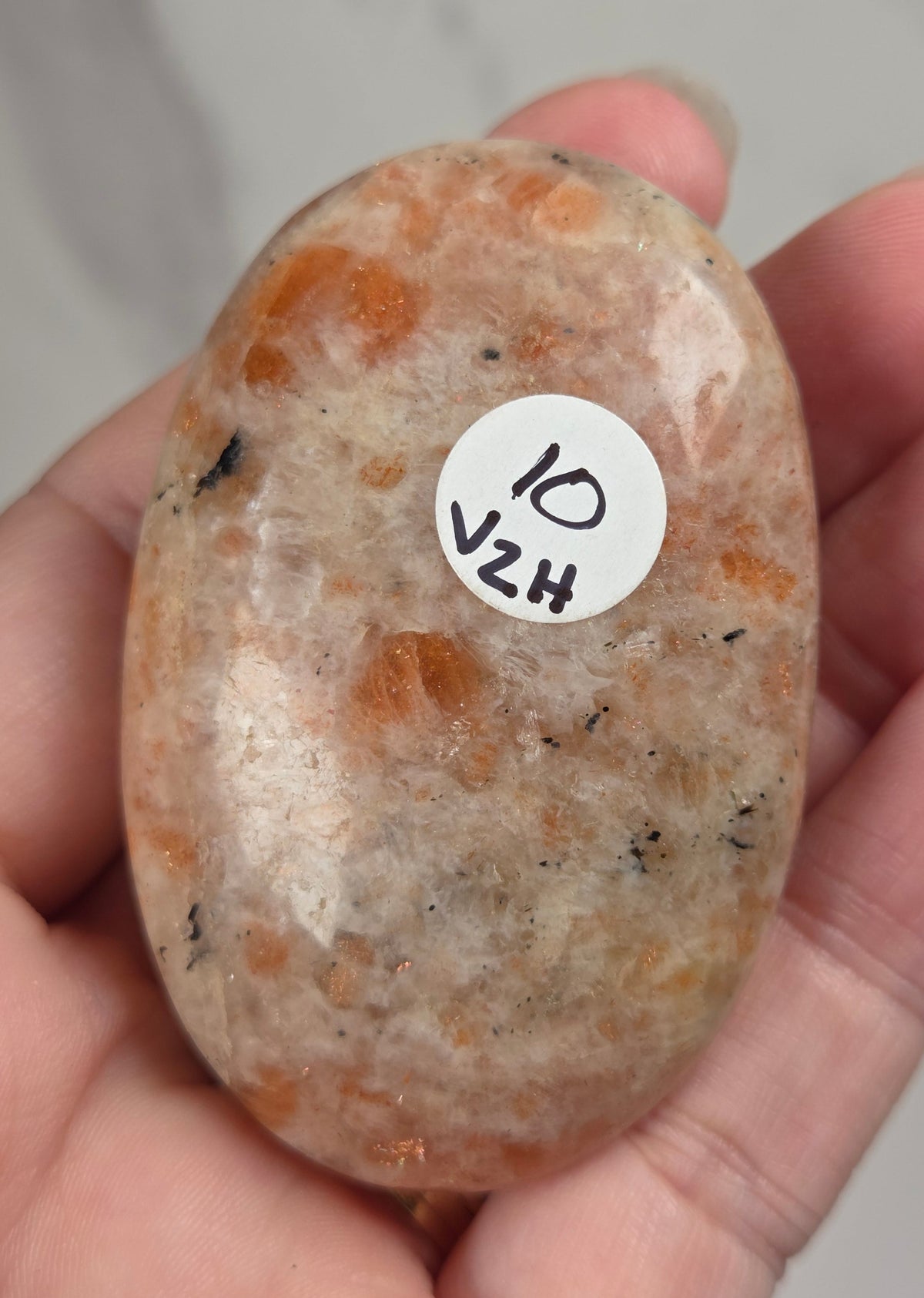 Polished orange sunstone free form carving being held in a hand against a marbled background