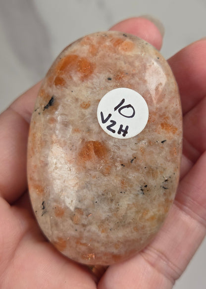 Polished orange sunstone free form carving being held in a hand against a marbled background