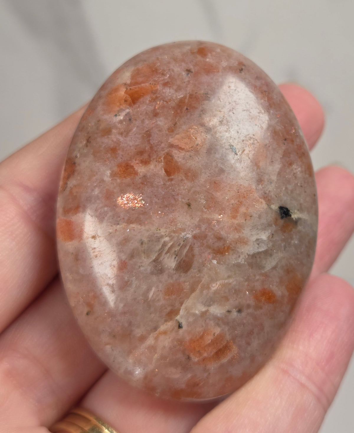 Polished orange sunstone free form carving being held in a hand against a marbled background