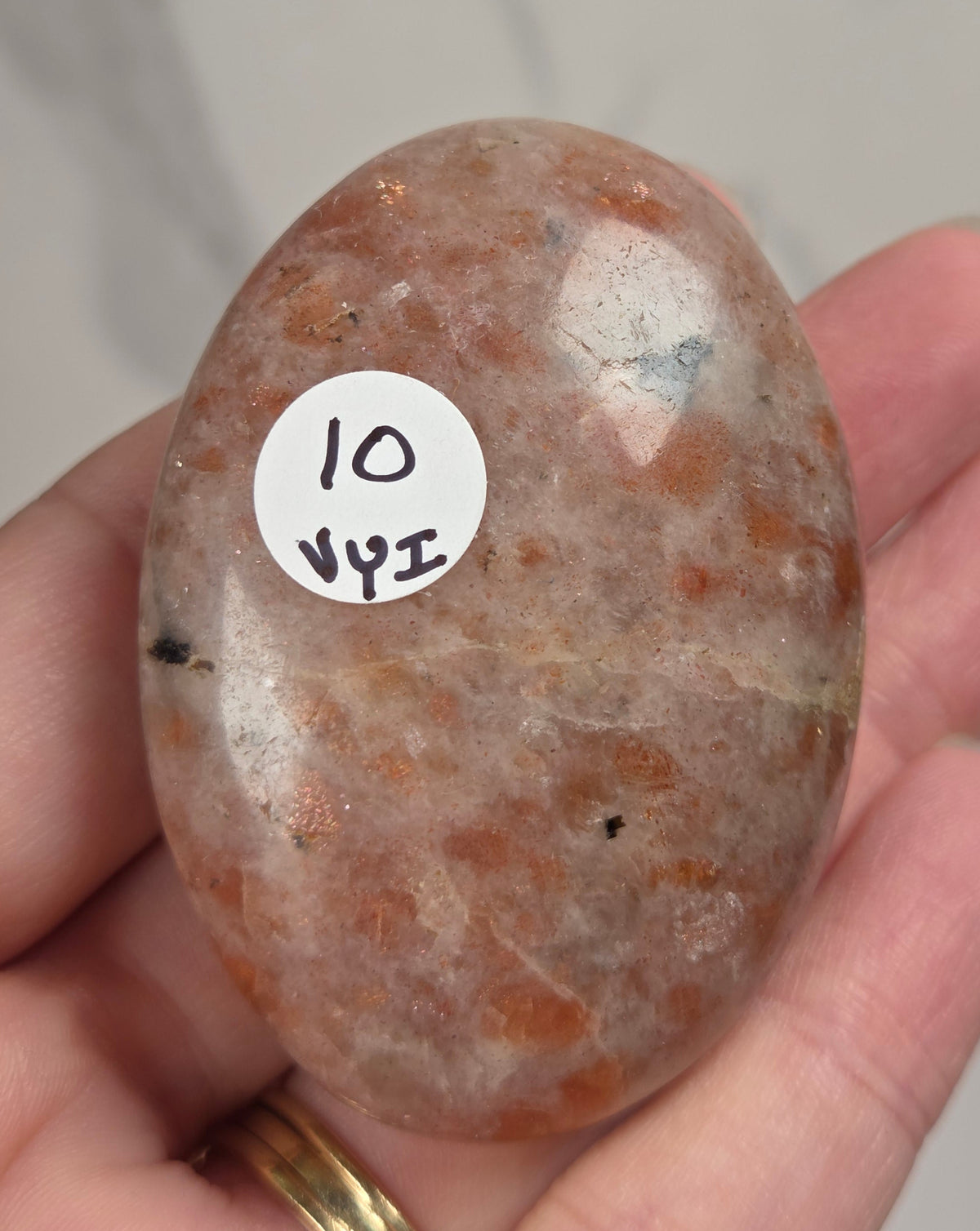 Polished orange sunstone free form carving being held in a hand against a marbled background